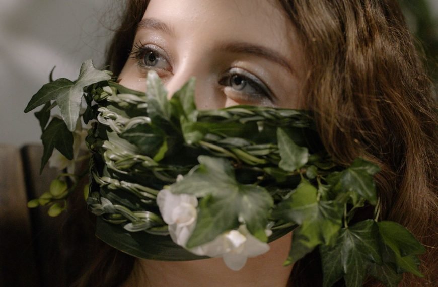 A woman's face adorned with a creative mask made of green leaves and flowers.