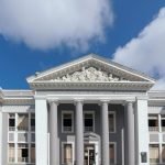 A classical building facade featuring tall pillars and ornate detailing against a blue sky.