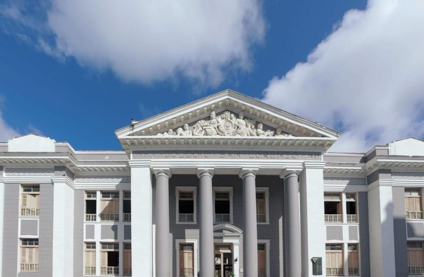 A classical building facade featuring tall pillars and ornate detailing against a blue sky.