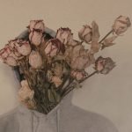 Artistic photo of a person with a bouquet of withered roses covering their face, wearing a hoodie.