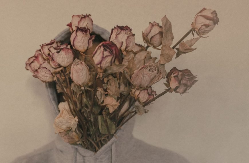 Artistic photo of a person with a bouquet of withered roses covering their face, wearing a hoodie.