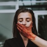 A creative portrait of a woman with a painted hand covering her mouth, conveying mystery and depth.