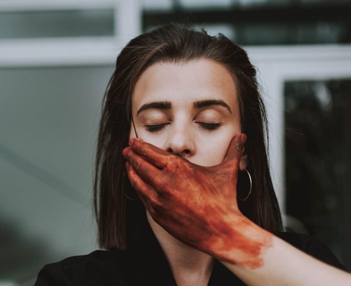 A creative portrait of a woman with a painted hand covering her mouth, conveying mystery and depth.