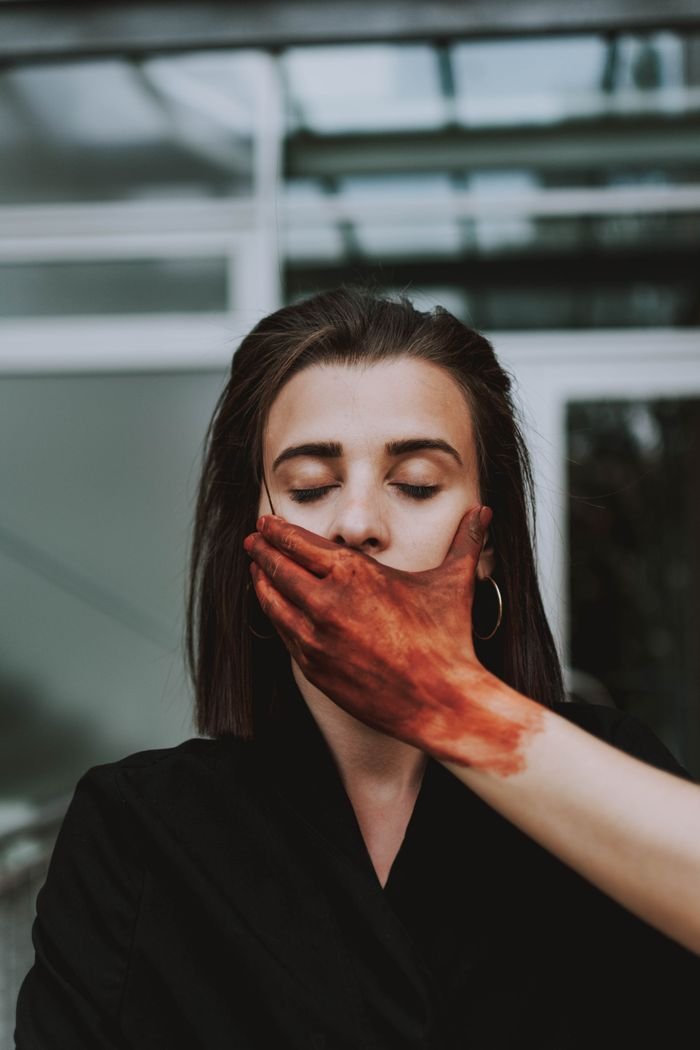 A creative portrait of a woman with a painted hand covering her mouth, conveying mystery and depth.