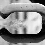 Black and white image of a pipe creating ripples in water. An abstract reflection scene.
