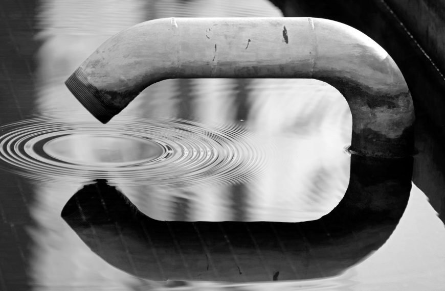 Black and white image of a pipe creating ripples in water. An abstract reflection scene.