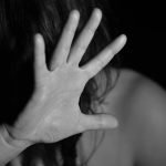 A black and white photo of a woman raising her hand, obscuring her face, suggesting a stop gesture.