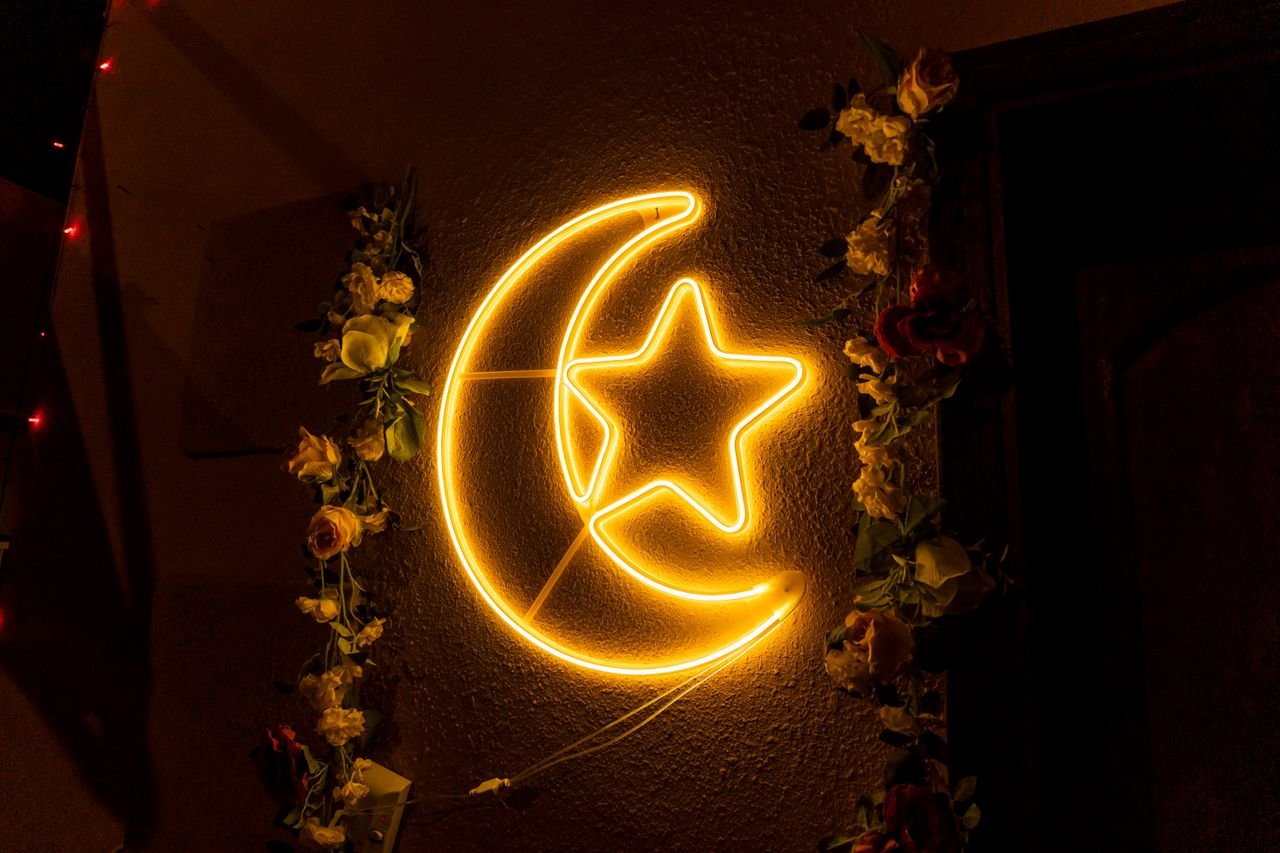 Neon crescent moon with star and floral garland, ideal for festive decor.