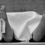 Conceptual black and white photo with symbolic 'Game Over' tag on feet.